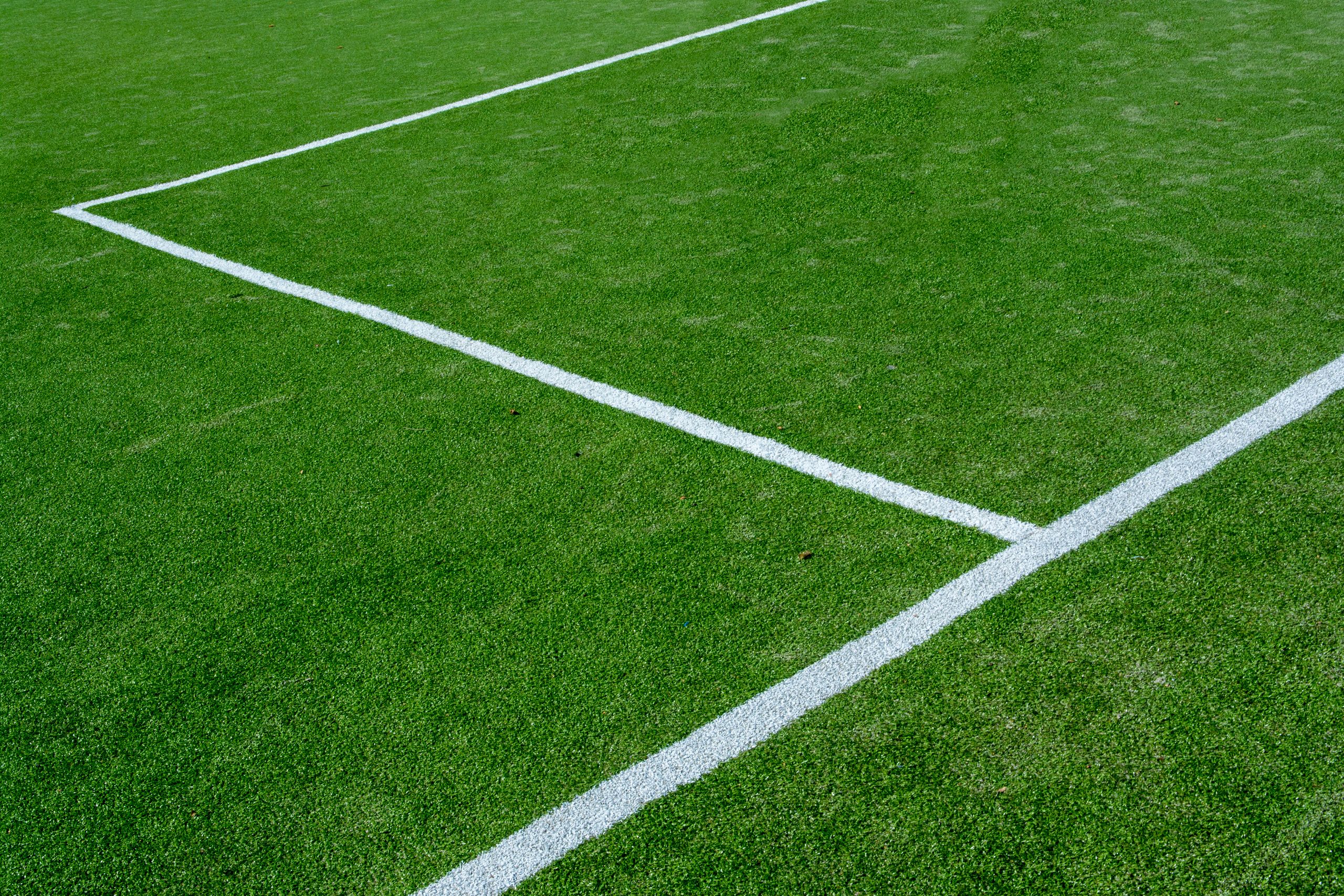 A sharp corner of a soccer field with green grass and crisp white lines.